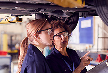 mentor mechanic guiding apprentice under car