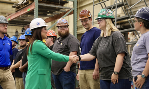 Secretary Chavez-DeRemer, wearing a hard hat, shakes hands with a woman in the trades while several other workers look on