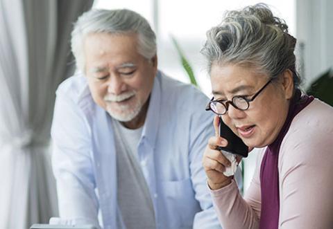 An elderly couple on the phone, looking at a laptop (off-screen)