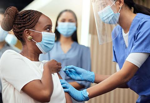 A masked woman getting the COVID-19 vaccine from a masked health worker