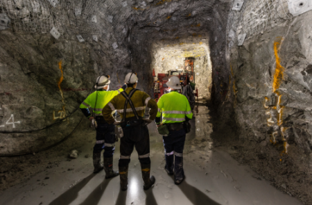 Three workers in an underground mine. All are wearing helmets and reflective gear.