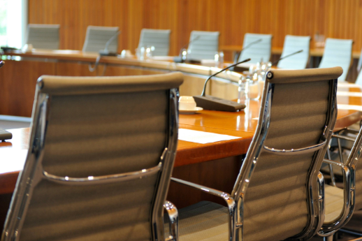 One section of a large curved dais desk ringed with beige leather office chairs in a wood-paneled conference room.