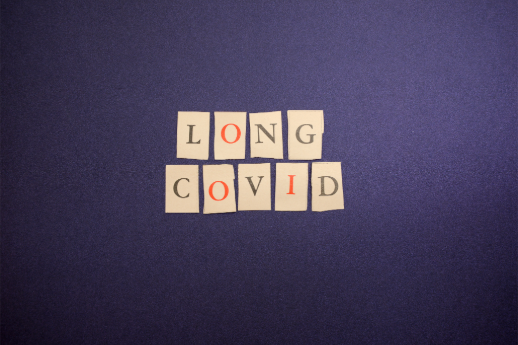 Red and black block letters printed on slips of paper, reading LONG COVID, on a dark blue background.