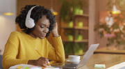 A woman wearing headphones takes notes during an online training course. 