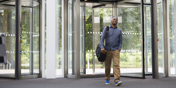 A man carrying a briefcase enters a building through a revolving door.