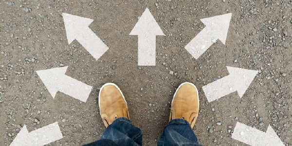 Concept: Moving forward. Close-up of a persons shoes on a gravel path, with arrows leading in several directions.