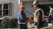 Two men shake hands outside a storm-damaged house. One wears an OSHA protective vest, as well has gloves and hard hat.