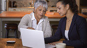 Two women review information on a laptop.   