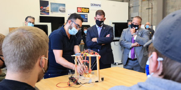 Secretary Walsh observes college students showing a tool they've engineered.