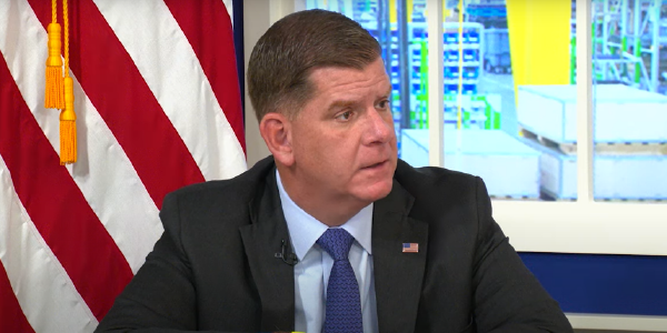 Secretary Walsh sits in front of an American flag at a White House event. 