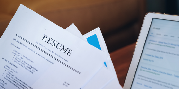 A pile of resumes fanned out in front of an open laptop. 