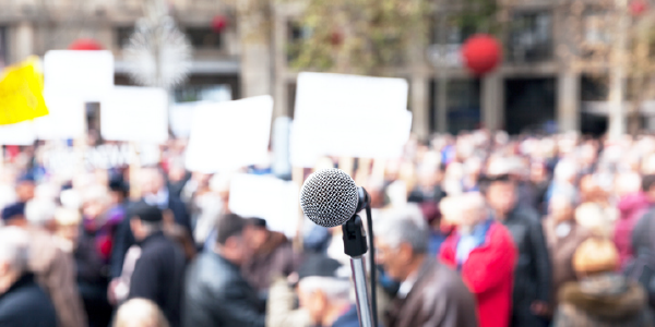 A microphone in the foreground, with a crowd of people in the background.