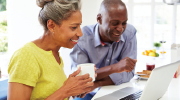 An older couple smiles while looking at an open laptop. 