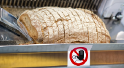 A loaf of bread goes through a bread slicer. The machine has a warning label on it. 