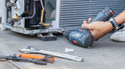 Close-up shot of an HVAC technicians hand holding a drill near an AC unit.