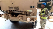 A service member in safety gear stands in front of a military vehicle.