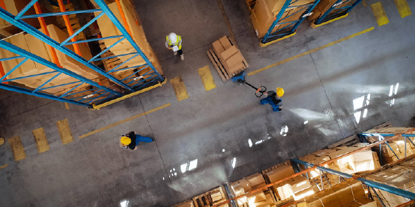 Top-down view of three workers in safety gear moving a pallet in a warehouse.