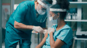 A medical practitioner vaccinates a colleague in a medical setting. 