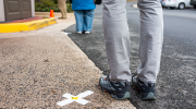 Three people stand in a line, near tape Xes, six feet apart. 