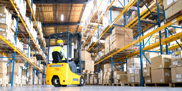 A man in safety gear operates a forklift in a warehouse. 