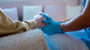 A home healthcare worker in surgical gloves holds the hand of an elderly patient. 