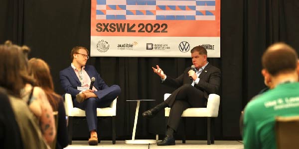 Secretary Walsh speaks during an interview on a stage with a SXSW 2022 sign in the background.