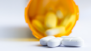 Close-up of a group of white tablets with an out-of-focus prescription bottle in the background.