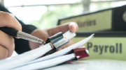 A stack of business papers in front of two binders labeled salaries and payroll.