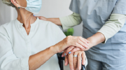 An older woman in a chair turns toward a female care worker in scrubs.