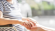 A person in a wheelchair holds the hands of an assistant.