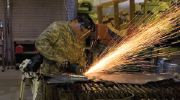 A U.S. Army Specialist grinds a stack of metal sheets using a circular grinder, sending up sparks. Photo by Sgt. Gustavo Olgiati.