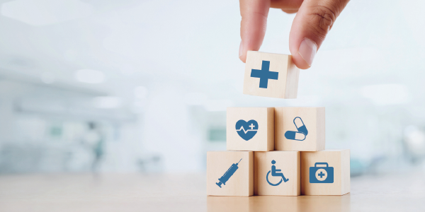 A stack of blocks bearing health icons a medical cross, a heartrate symbol, pills, a syringe, a handicap sign and a medical bag.