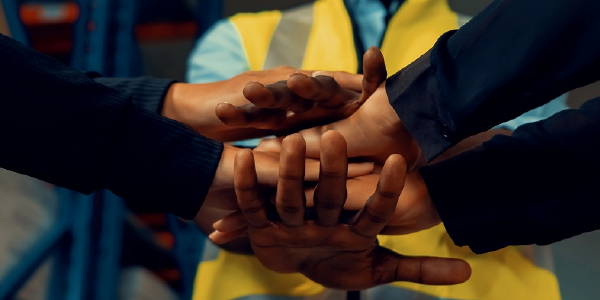 A pair of hands overlapping with each other with an individual in the background with a yellow vest. 