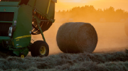 A hay baler and a freshly rolled haybale in a misty field.