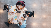 Five college-aged students sit around a circular table covered in books, laptops and notebooks. 