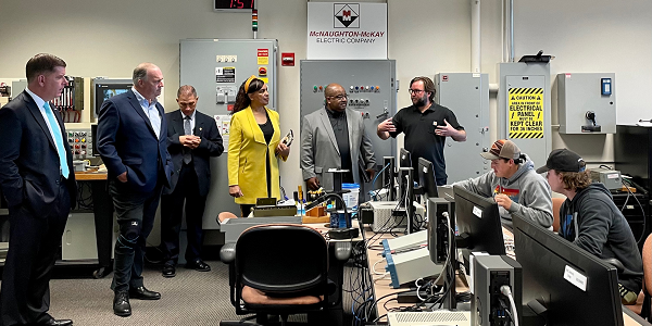 Secretary Walsh and Rep. Dan Kildee meet with staff and students at a Mott Community College training facility. Several students are working at computer stations and electrical equipment is in the background.