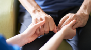 A close up of hands. A younger person holds an older personâs hands in their lap. 