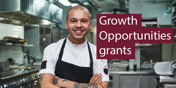 Photo of young man smiling in a restaurant kitchen. Text reads: Growth Opportunities grants.