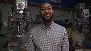 Ron Vargas stands, smiling, in a training facility with manufacturing machinery and tools in the background 