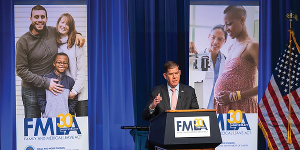 Secretary Walsh speaks at a podium. Behind him are banners featuring happy families, bearing the FMLA 30th anniversary logo.