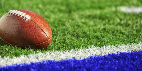 A football rests on a football field. The grass is striped with white and blue paint.