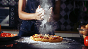 Flour floats through the air as a worker prepares a small pizza.