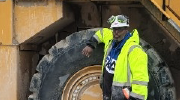 A man stands in front of a large vehicle wearing a hardhat 