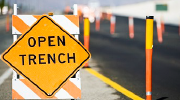 A traffic sign reading open trench stands by the side of a paved road.