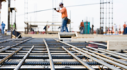 A construction worker carries a metal bar across a worksite.