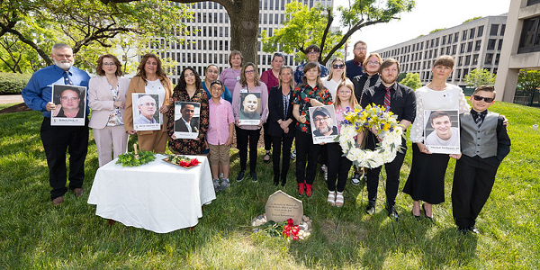 OSHA Family Liaison Tonya Ford and family members of workers killed on the job gather outside around the Labor Department's memorial to fallen workers. Several hold photos of their lost loved ones. 