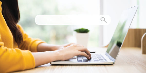 A woman sits in front of a laptop opened to a search window, prepared to type.