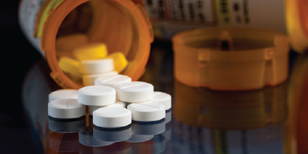 An open prescription pill bottle, with unlabeled white pills spilling out of it.