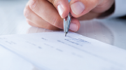 Close-up of a hand signing a check.