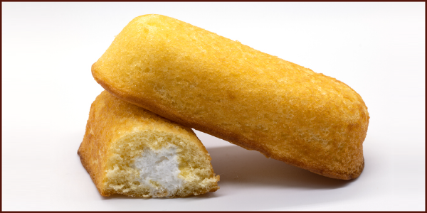 Two Twinkie snack cakes â one whole, one sliced in half to reveal the creamy center.